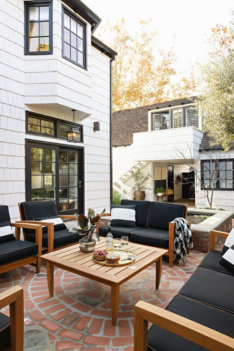 Des sièges et divans noirs sur un pavé de briques rouges. Apparence rustique et chaleureuse. Crédit à Better Homes & Gardens.